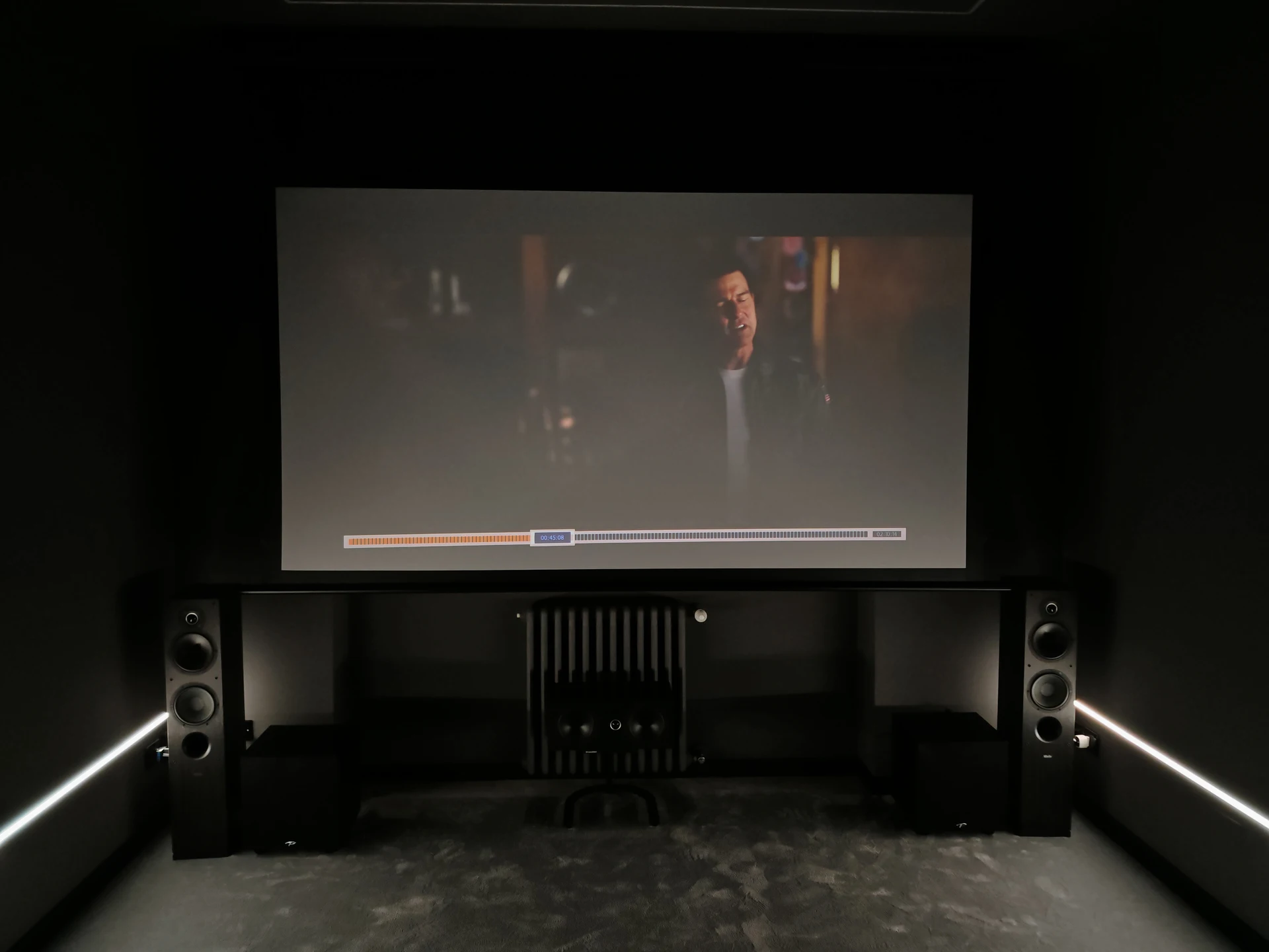 Fronte cinema di Volpiano con schermo in proiezione, due diffusori frontali e due subwoofer.